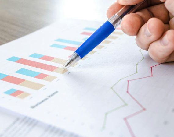 Hand holding a pen over business charts and analytics, symbolizing cloud communication strategies for business growth.