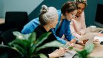 Three women in a strategic meeting discussing a VoIP and IoT business strategy in a modern office setting.
