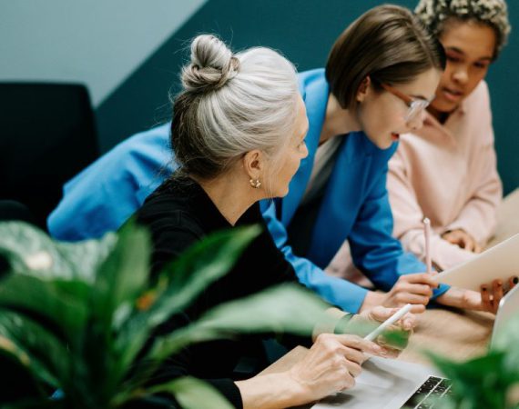 Three women in a strategic meeting discussing a VoIP and IoT business strategy in a modern office setting.