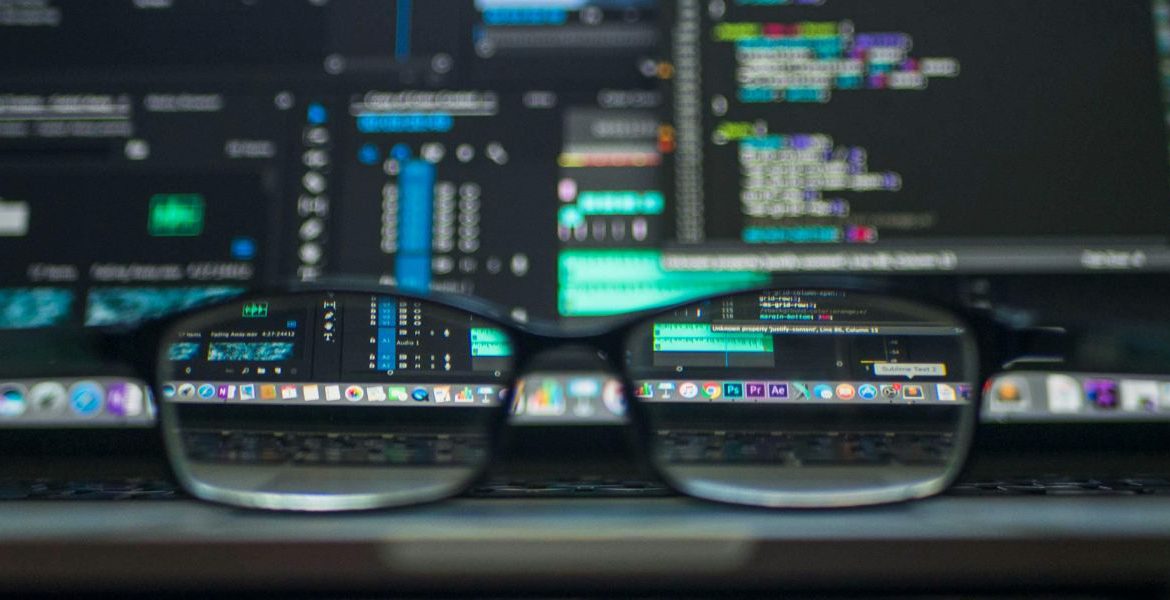 Close-up of glasses in front of dual monitors displaying lines of code, symbolizing VoIP and IoT strategic planning for secure and intelligent network integration.
