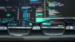 Close-up of glasses in front of dual monitors displaying lines of code, symbolizing VoIP and IoT strategic planning for secure and intelligent network integration.