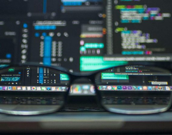 Close-up of glasses in front of dual monitors displaying lines of code, symbolizing VoIP and IoT strategic planning for secure and intelligent network integration.