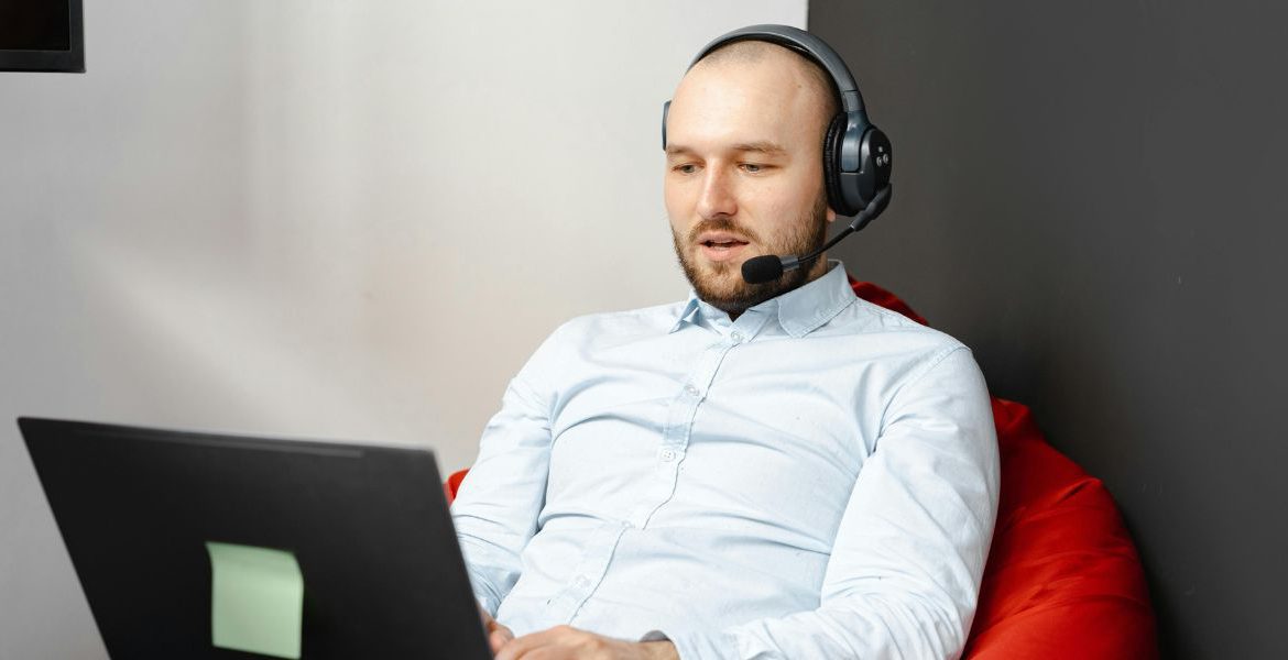 Man using VoIP on a laptop with a headset, benefiting from VoIP Quality of Service (QoS) for clear and reliable communication.